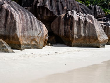 A pristine empty white sand beach in the Seychelles, framed by massive smooth granite boulders, dramatic sunlight, wide shot.