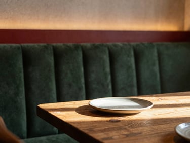 Cozy Scandinavian-style restaurant interior, soft warm overhead lighting, rustic wooden table with a single ceramic plate, moody shadows