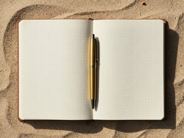 Overhead flat-lay of a high-quality open linen notebook with clean, empty grid pages, a single brass pen resting in the center fold, soft morning light casting long gentle shadows across a warm sand surface.