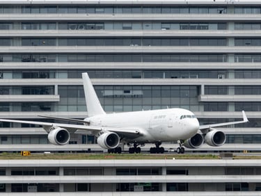 High-capacity cargo aircraft on a runway at an international airport under overcast daylight, wide-angle architectural framing, cool industrial photography, desaturated steel tones, sharp focus, 35mm