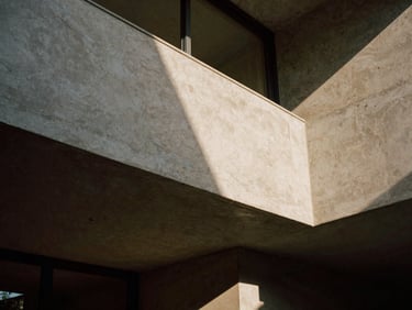 Dramatic architectural elevation of a concrete and travertine residential interior, sharp low-angle window light casting long shadows, medium format film