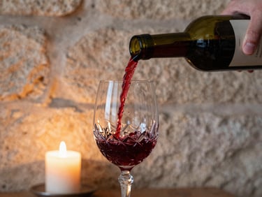 Somatic close-up of red wine being poured into a crystal glass in an old stone cellar, soft candlelight