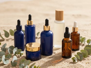 A beautiful arrangement of organic skincare bottles and fresh eucalyptus leaves on a soft sand surface, natural light