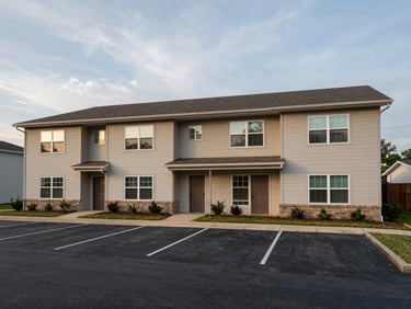 Wide exterior of a four-unit residential rental property in Springdale AR, two-story building, separate entry doors visible, overcast afternoon light, parking area in foreground, observed street-level framing