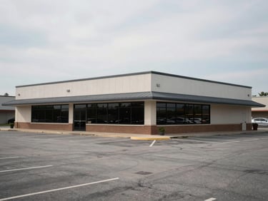 Wide exterior of a small commercial strip building in Bentonville AR, flat facade, parking lot in foreground, overcast midday light, real street-level perspective, no signage