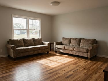 Interior wide shot of a modest living room in a northwest Arkansas home, natural window light falling across hardwood floors, neutral walls, real furniture in place, slightly overcast daylight, no staging props, honest proportions visible