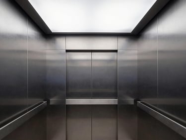 Interior of a clean modern elevator cabin, brushed steel panels, minimalist LED ceiling lighting, sharp architectural framing