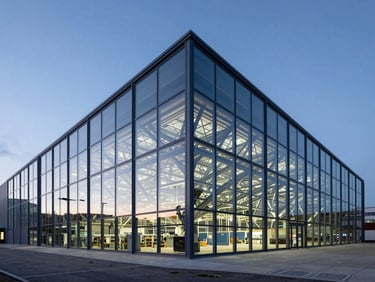 Wide architectural shot of a modern glass logistics terminal in London at dusk, cool blue daylight, geometric steel frames reflecting global connectivity.