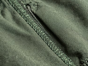 Macro shot of custom stitching on a heavy-duty canvas jacket, pine green thread, natural daylight.