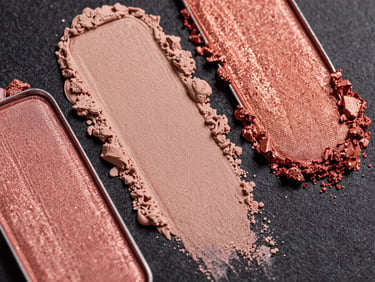 Macro close-up of vibrant rose gold and nude powder eyeshadow swatches on a dark textured surface.
