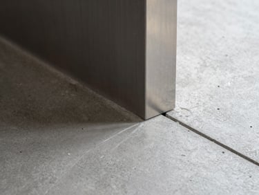 Detail shot of a perfect material transition, where a polished concrete floor meets a brushed steel profile with a clean, razor-sharp joint, bright natural architectural lighting.