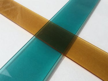 An abstract geometric composition of intersecting teal and amber translucent planes, casting sharp architectural shadows on a clean white surface, daylight.