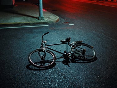 Cinematic shot of a single retro bicycle lying abandoned on a dark, wet asphalt road under a pale blue streetlamp, heavy shadows, film grain