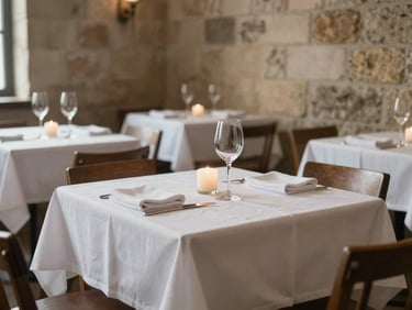 Empty restaurant dining room before service, white-linen table with wine glass and single candle, stone walls, northern natural light, no people