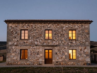 Stone facade of a rural hotel in Castilla y León at dusk, warm interior light through windows, austere landscape in background, no people