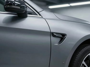 Close-up of a sharp, deep dent on a metallic grey car door panel under bright clinical workshop lighting.