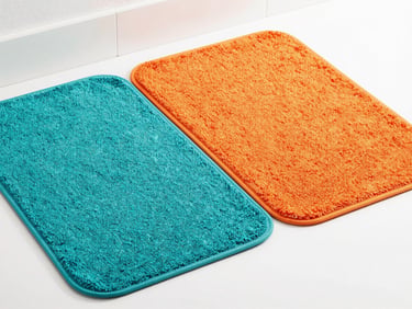 Two matching bath mats, one teal and one orange, neatly folded in a modern bathroom setting, bright studio light, 35mm