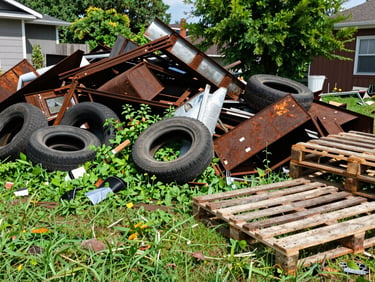 Before: A messy suburban backyard overgrown with weeds, piled high with rusty scrap metal, old tires, and broken wooden pallets.