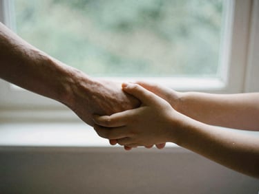 A close-up of two hands, one adult and one child, holding hands gently, soft focus, natural window light, stone tones.