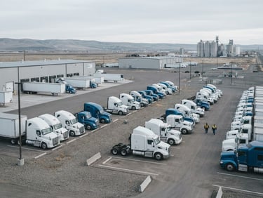 A wide-angle environmental photograph of a clean regional transport yard in Pasco, Washington, with fleet trucks parked under soft overcast daylight, cool desaturated tones, sharp focus, 35mm lens.