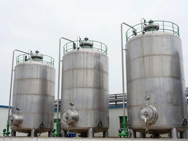 Wide environmental photography of modern chemical reactors and stainless steel storage tanks under clean, bright overcast sky, sharp focus, clinical precision
