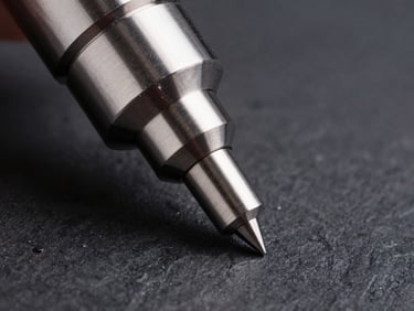 Extreme macro photography of a CMM probe touching a precision-milled aerospace component, cool directional highlights on the metal surface against a dark slate background.