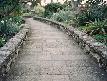 Historic stone pathway winding through an Acadian garden, soft morning light, weathered textures, quiet editorial photography