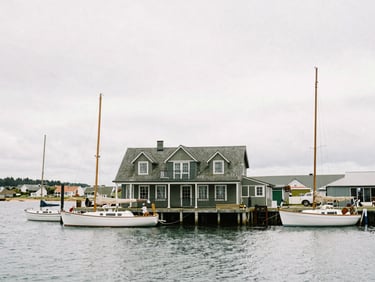 Historic harbor master's residence overlooking a calm working harbor with wooden sailboats, soft overcast daylight.