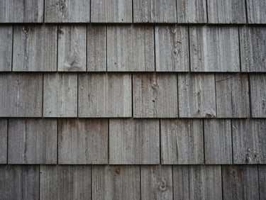 Close-up of weathered cedar shingles on an old boathouse, textured, muted gray-browns, soft overcast light