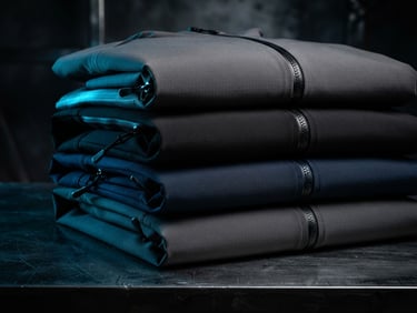 Sleek editorial product photography of minimalist technical jackets stacked neatly on a dark steel surface, sharp high-contrast studio lighting, electric blue gel accents, 50mm lens.