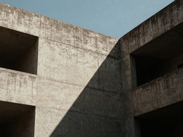 Low angle shot of brutalist concrete architecture, sharp diagonal shadow cutting across the frame, clear sky.
