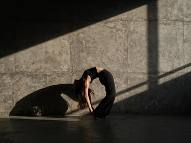 High-contrast wide shot of a dancer arching their back against a raw concrete brutalist wall, dramatic low-key natural light, deep shadows, cinematic composition.