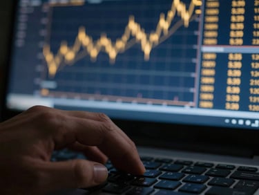 Close-up of a hand on a keyboard, with reflections of golden-lit financial charts on a dark screen, editorial photography