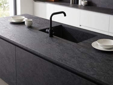 Close-up of a minimalist luxury kitchen island, dark anthracite stone surface, matte black faucet, elegant ceramic tableware, bright natural daylight.