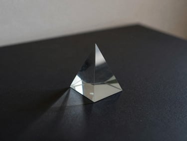 A minimalist abstract image of a dark glass prism refracting a single ray of light into scattered patterns on a black surface, soft shadows.