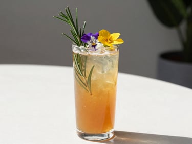 Vibrant amber non-alcoholic mocktail garnished with fresh rosemary sprigs and edible wildflowers, bright natural daylight, clean modern composition