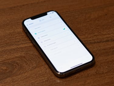 Android phone lying flat on a wooden desk in clean studio light, screen showing a minimal productivity app with clear task rows and a teal checkmark, top-down close-up shot