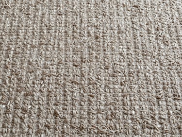 Overhead close-up of a wool carpet section laid flat, texture detail visible, natural daylight from above, no people