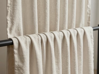 Close-up of heavy linen curtain fabric gathered on a workroom rail, natural daylight, muted off-white tone