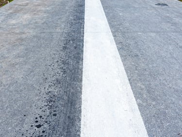 High-contrast split shot of a dirty concrete driveway being cleaned, showing a bright white restored path next to dark gray grime, sharp focus