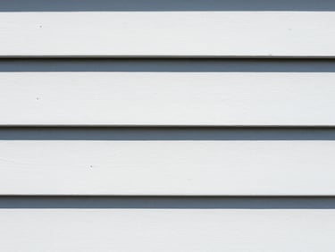 Tight macro shot of clean white vinyl siding next to weathered siding, bright midday sunlight, high contrast