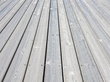 A clean wooden deck with pristine grain next to grey weathered wood, bright midday sun, crisp focus