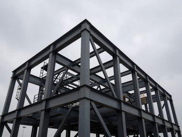 Low-angle wide shot of massive structural steel frames under dramatic overcast daylight, high-contrast steel and charcoal tones, industrial editorial photography, 35mm