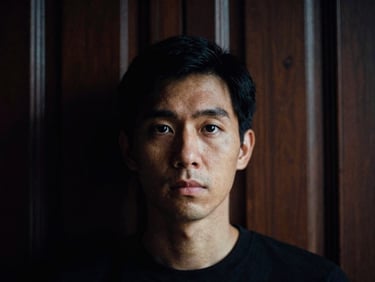 Close-up portrait of a designer with a focused expression, low-key dramatic side-lighting, dark wood paneled background, high contrast, 35mm film