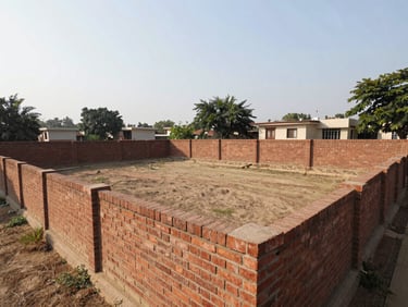 Bright wide-angle shot of a clean freehold residential plot of land in West Delhi, bounded by a neat brick wall