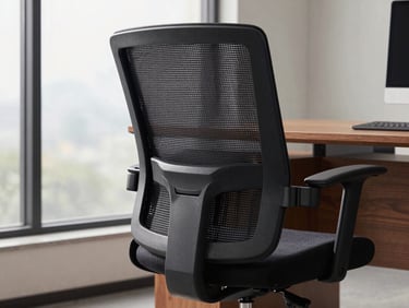 Detail shot of an executive office chair — dark charcoal mesh backrest and padded seat, lumbar adjustment mechanism visible, positioned at a wood desk, soft overcast daylight from a side window, no person seated, clean corporate setting