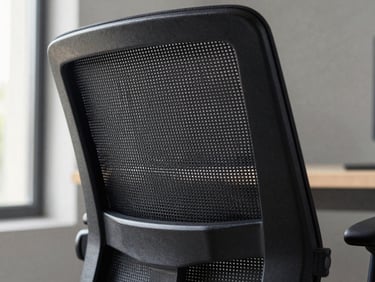 Close-up of an ergonomic executive office chair backrest, fine black mesh weave texture in sharp focus, aluminum armrest visible at the edge, soft natural window light from the left, neutral gray background, detail shot