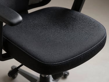 Close-up of an operational task chair seat cushion, dark charcoal fabric texture in sharp focus, visible stitching detail along the edge, soft diffused overhead light, studio material shot on neutral surface