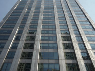 Low angle orthographic view of a modern Dubai commercial skyscraper facade, sharp glass panels reflecting direct desert daylight, clean structural lines, architectural steel gray tones.