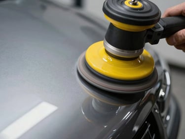Close-up of a multi-stage paint correction process, a professional rotary polisher on deep metallic paint, highlighting the boundary between micro-scratches and perfect reflection under a yellow inspection light.